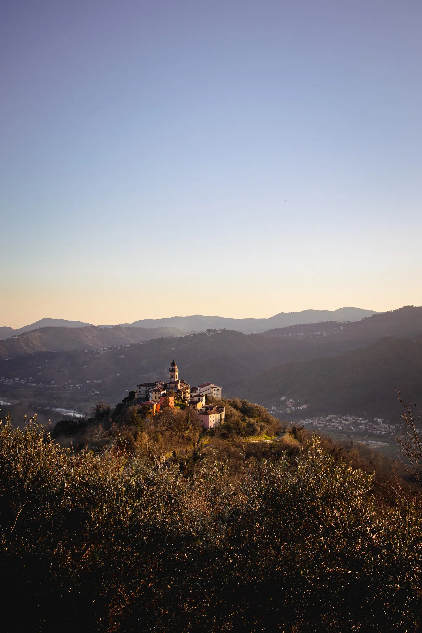 Borgo sulla cima di una collina alla luce del tramonto, con le montagne sullo sfondo