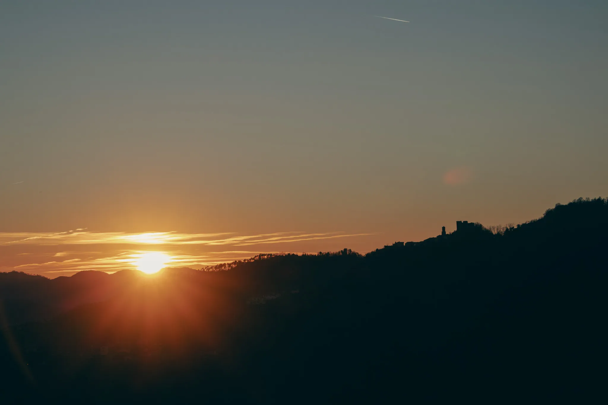 Sole che tramonta dietro il profilo scuro di una collina