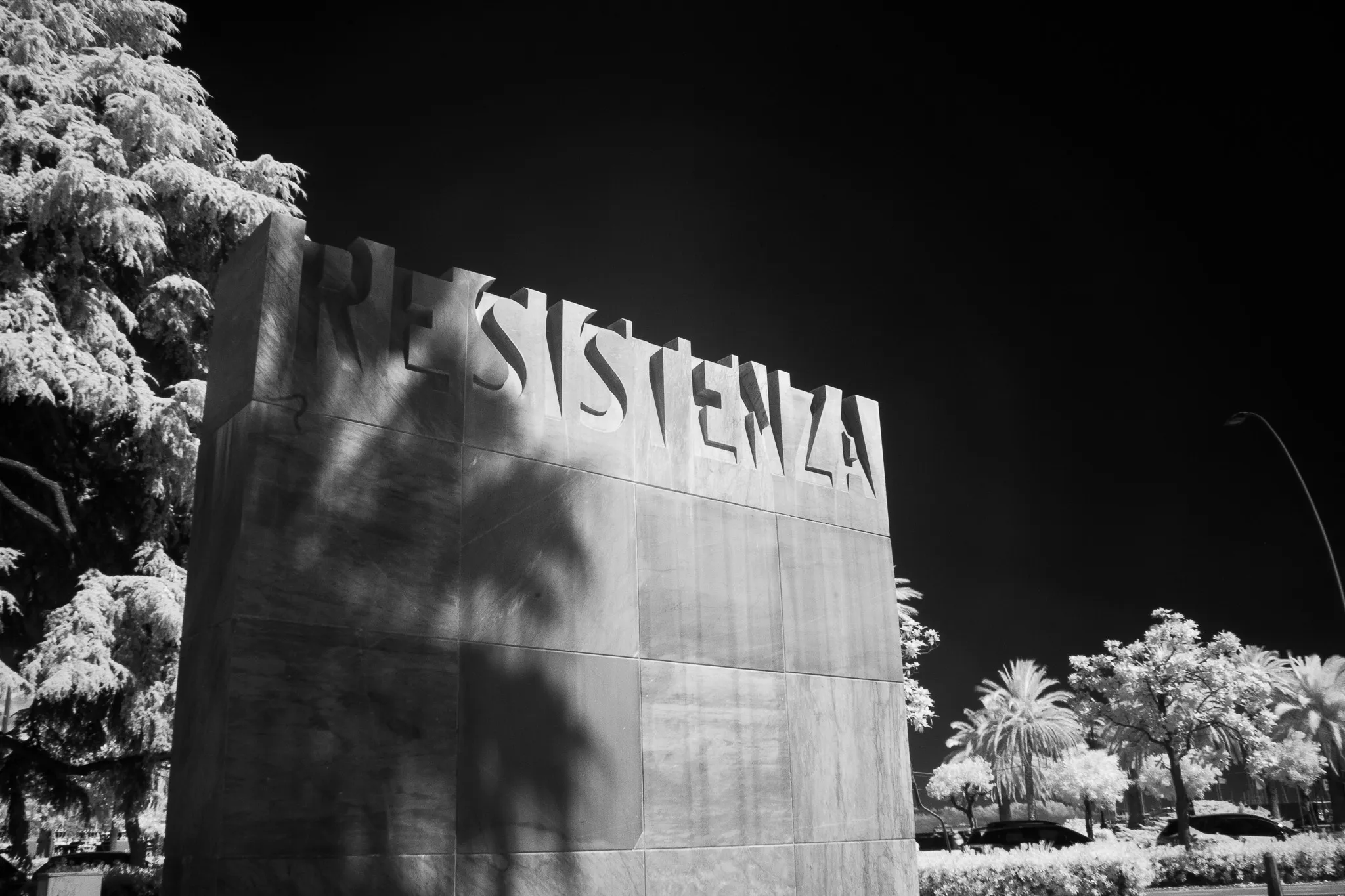 Monumento con la scritta Resistenza tra palme e alberi, in infrarosso bianco e nero