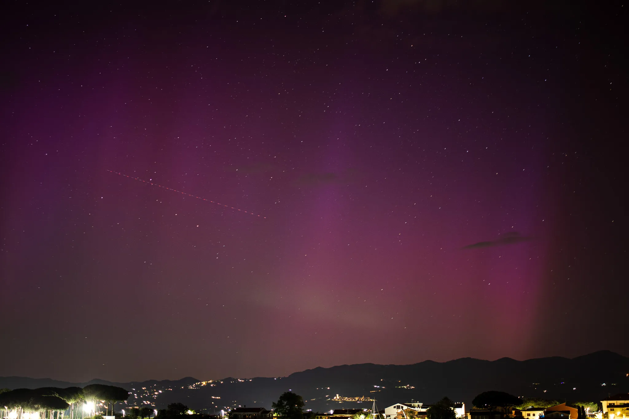 Aurora rosso-viola nel cielo notturno sopra le colline e le luci del paese