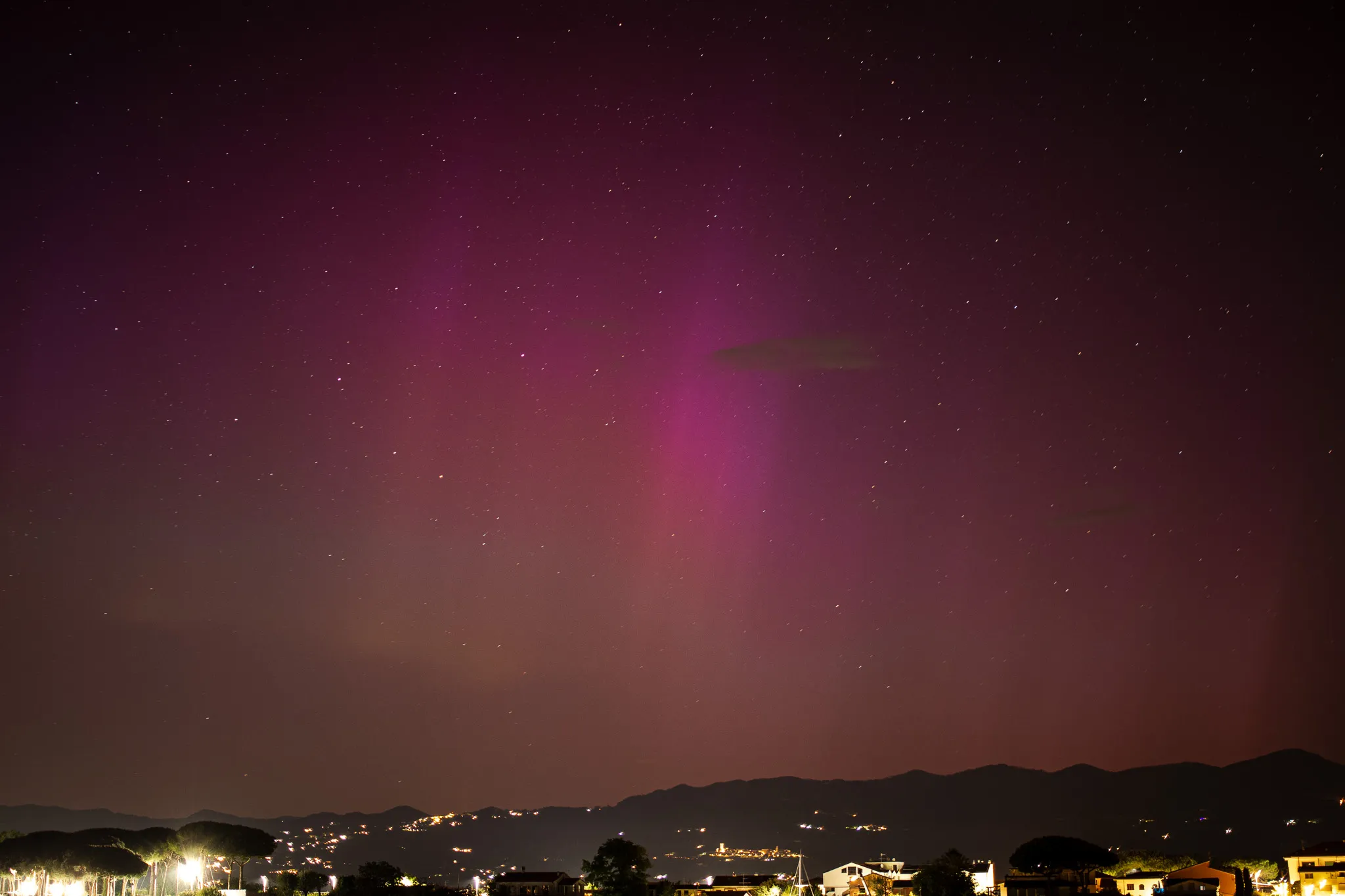 Aurora rosa intensa sopra il crinale, con le case illuminate in primo piano